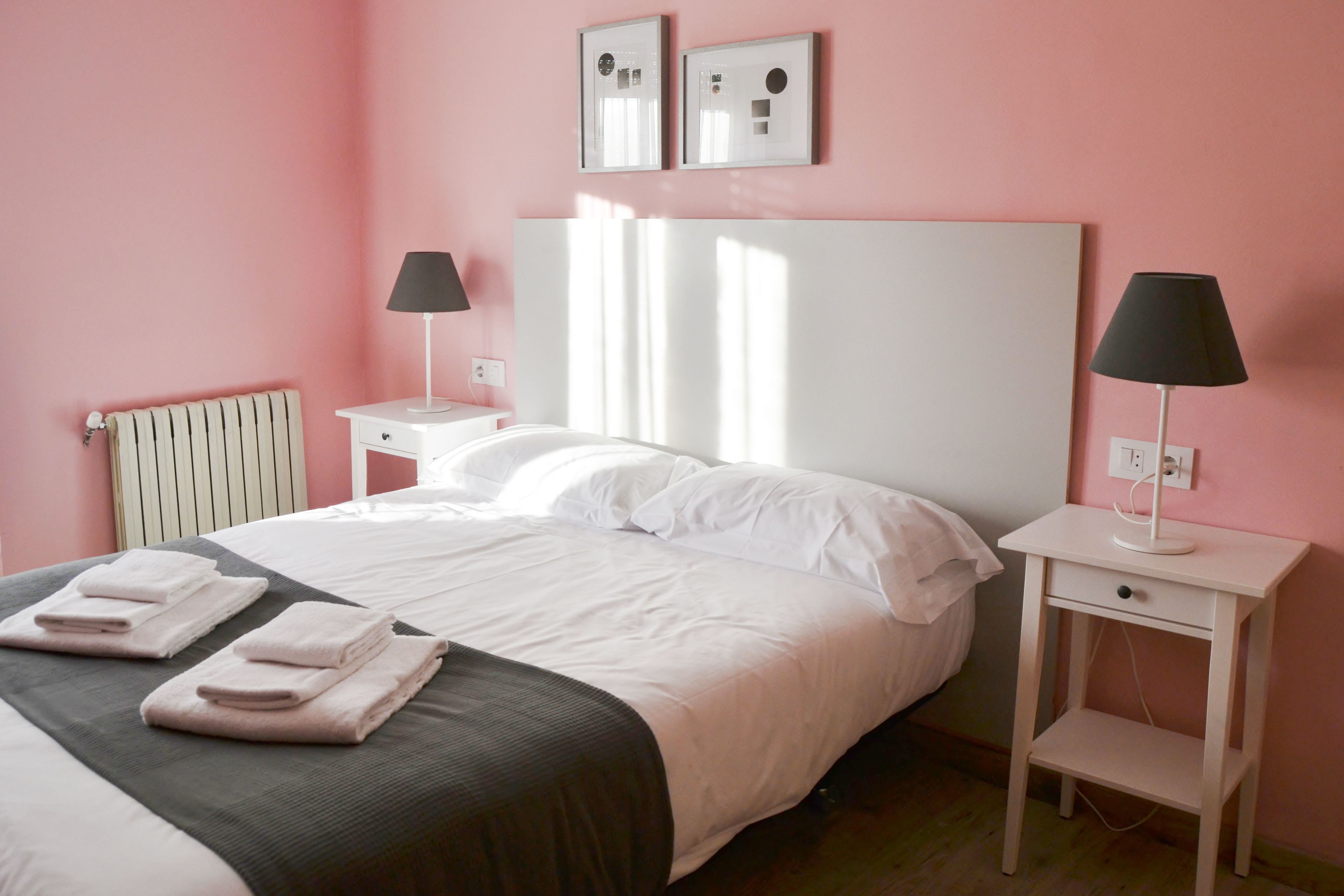 A neatly made bed with white linens and a dark gray bedspread, two bedside tables with lamps, and a radiator on the wall.