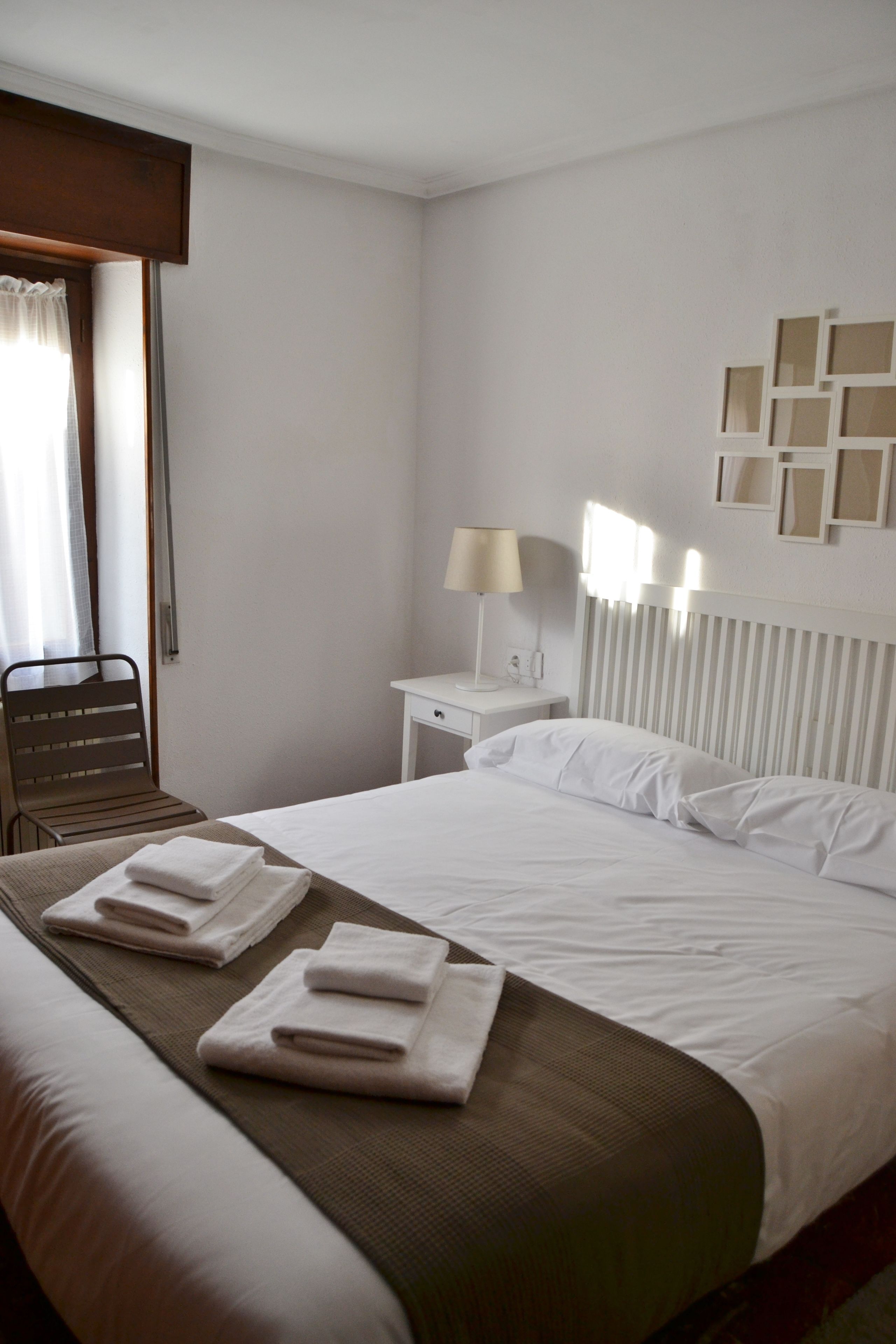 Een hotelkamer met een netjes opgemaakt bed, een stoel, een nachtkastje met een lamp en een muur met ingelijste foto's.