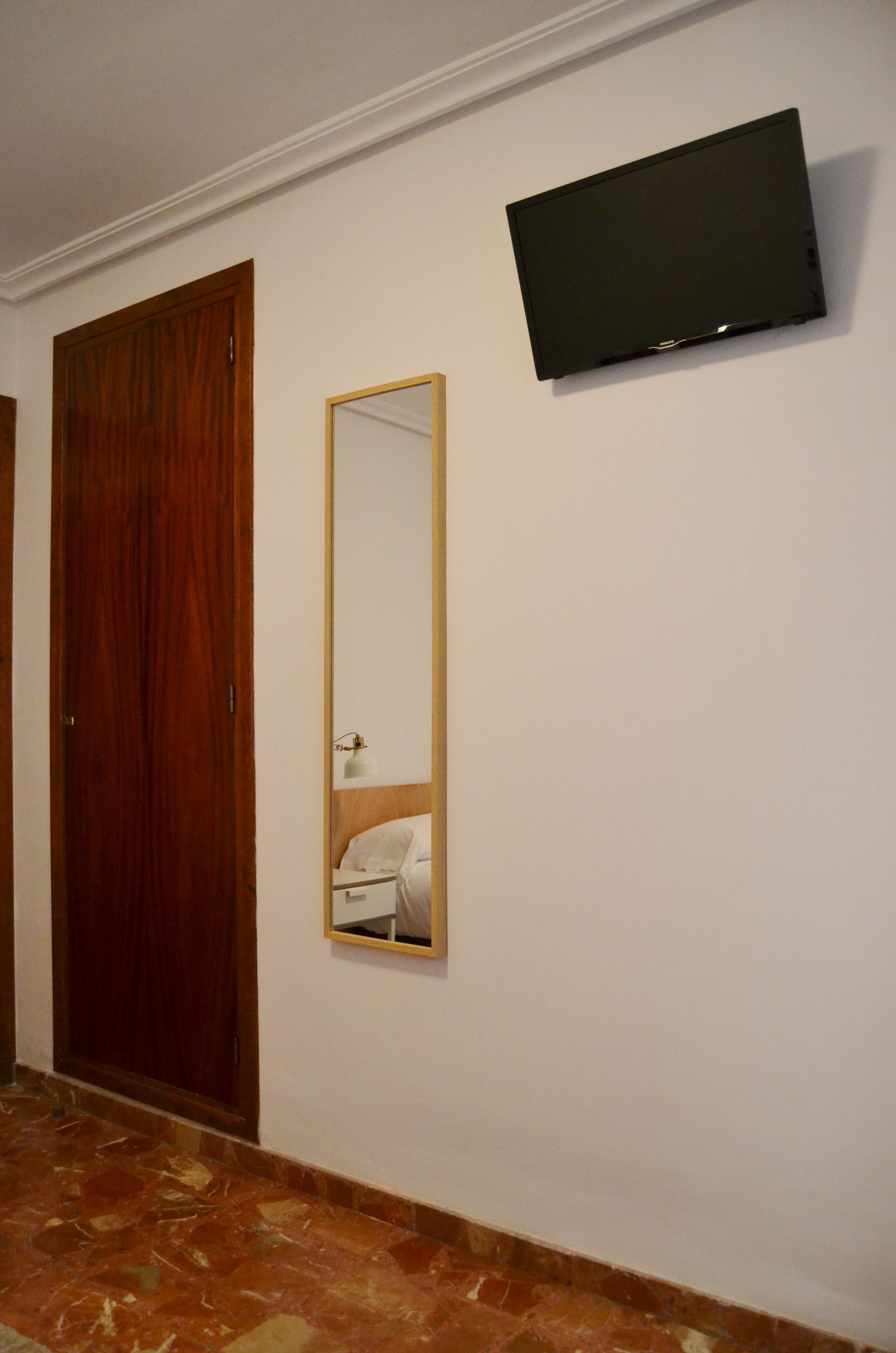 Un pasillo con puerta de madera, un espejo y un televisor montado en la pared.