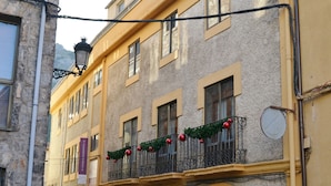 A yellow building with a balcony adorned with red ornaments and greenery. - Tres Puentes Anguiano (Anguiano)