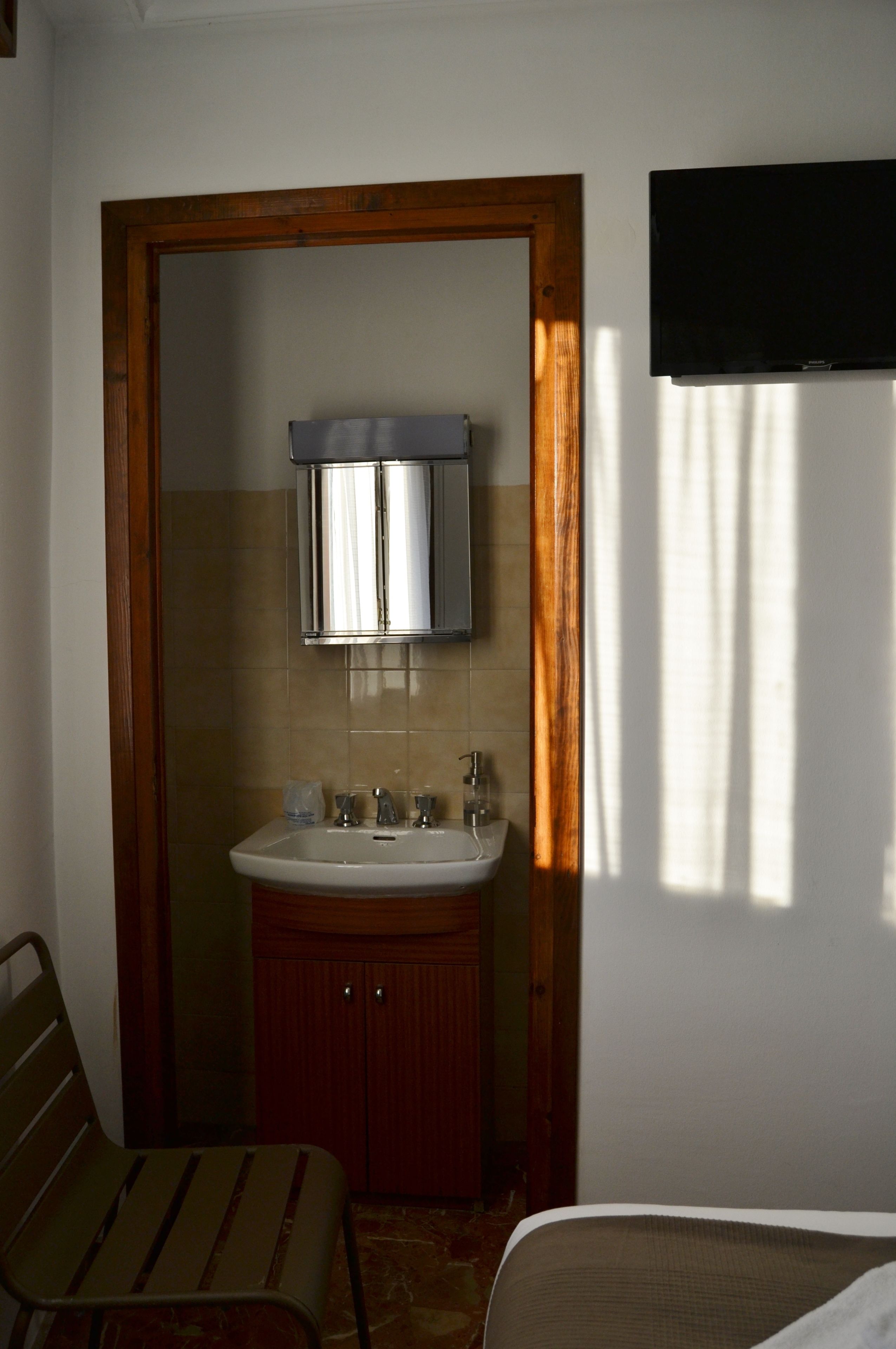 A bathroom with a wooden door, a sink, a mirror, and a television mounted on the wall.