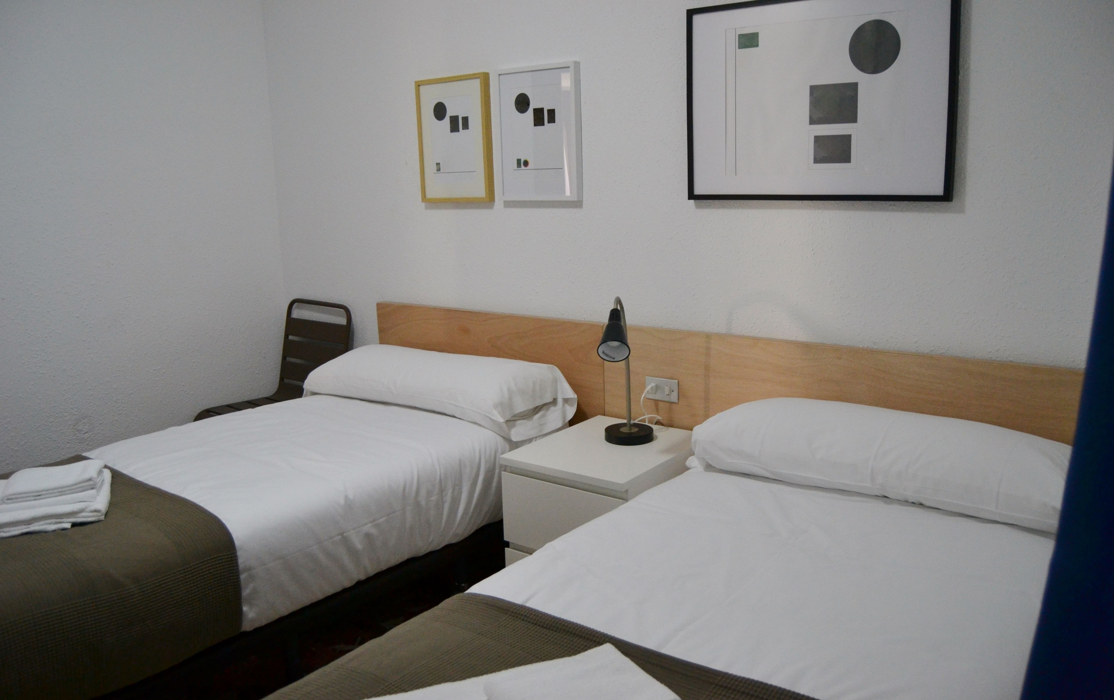 A hotel room with two beds, a nightstand, a lamp, and framed pictures on the wall.