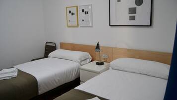 A hotel room with two beds, a nightstand, a lamp, and framed pictures on the wall.