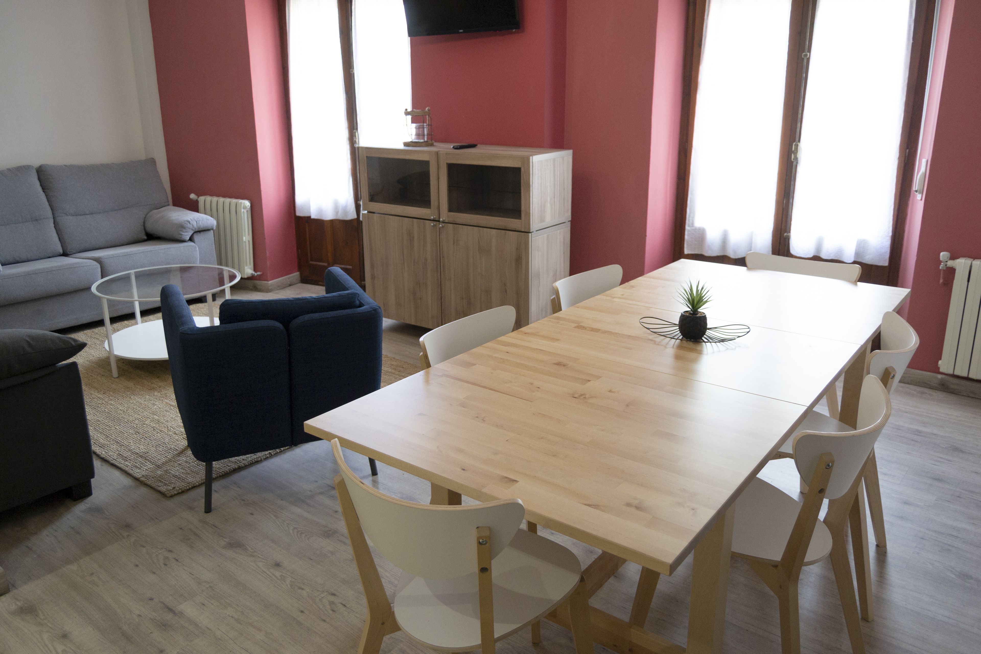 Una sala de estar moderna con una mesa de comedor de madera, sillas blancas, un sofá gris y un sillón azul.