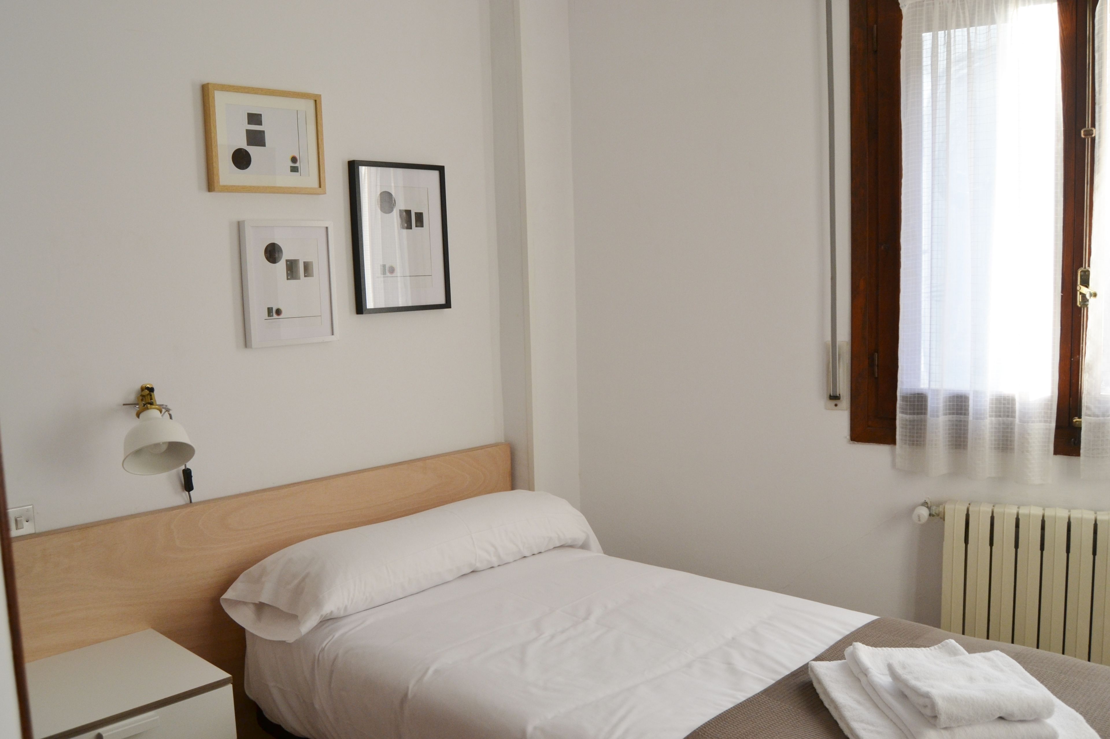 A neatly arranged hotel room with a bed, a bedside table, a lamp, and framed pictures on the wall.