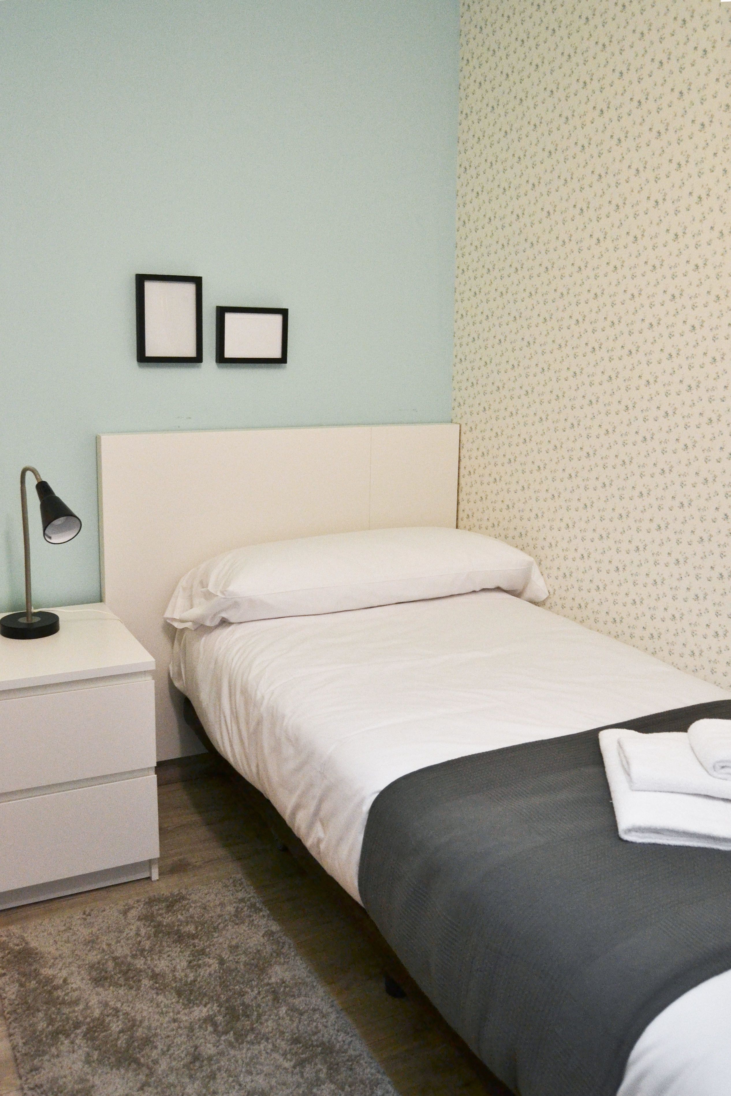 A neatly made bed with white bedding, a bedside lamp, and a small bedside table.