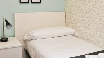 A neatly made bed with white bedding, a bedside lamp, and a small bedside table.