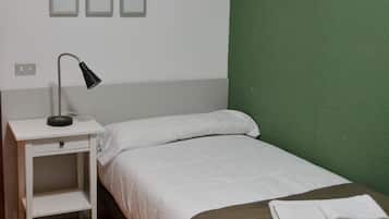 Una cama individual con ropa de cama blanca, una mesita de noche con lámpara y una pared verde.