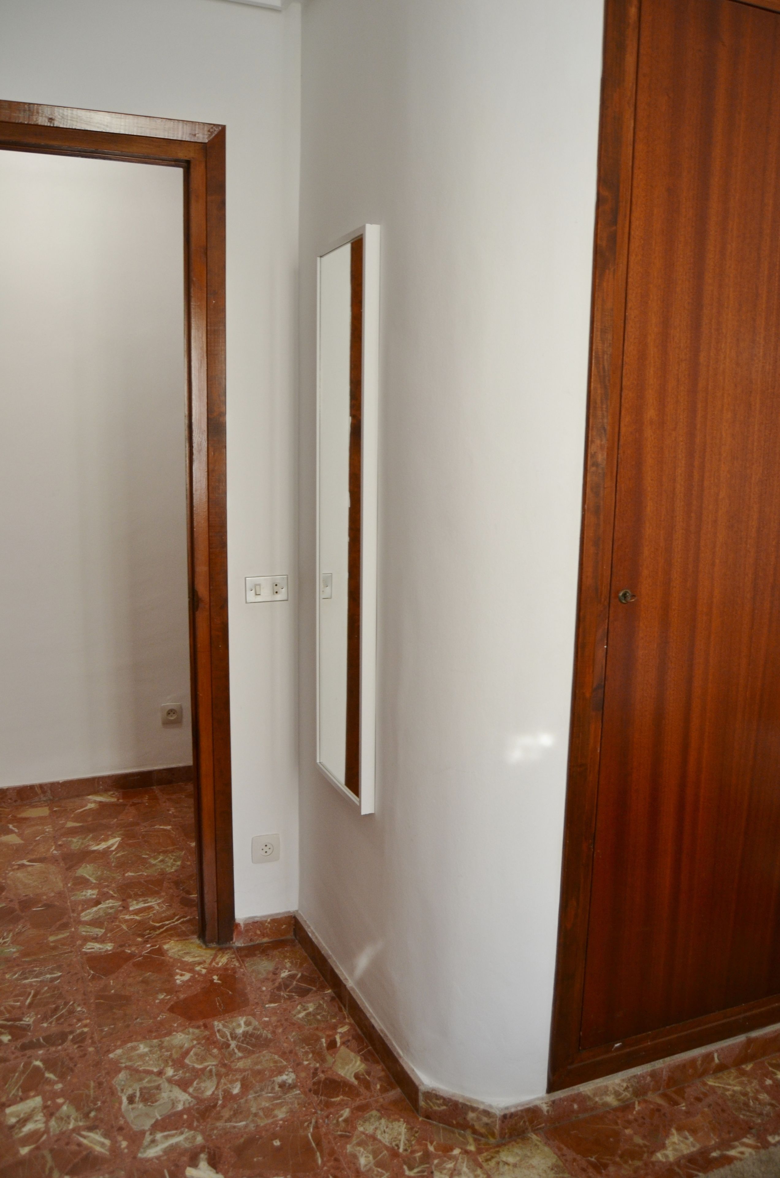 Un pasillo con una puerta de madera, una pared blanca y un armario de madera.