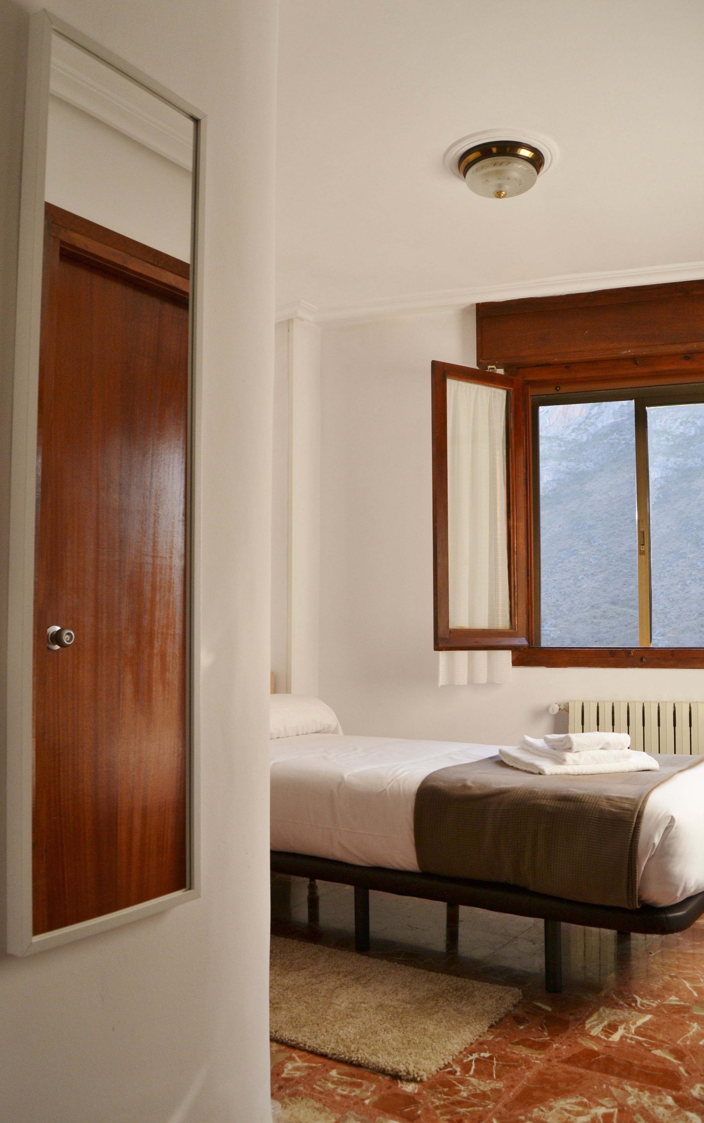 A bedroom with a wooden door, a bed with white bedding, a window with curtains, and a radiator.