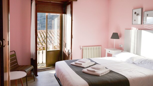 A bedroom with a bed, a chair, a nightstand, a lamp, and a window with a view of a balcony. - Tres Puentes Anguiano (Anguiano)
