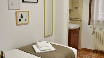 A hotel room with a bed, a bedside table, a mirror, and a bathroom visible through an open door.