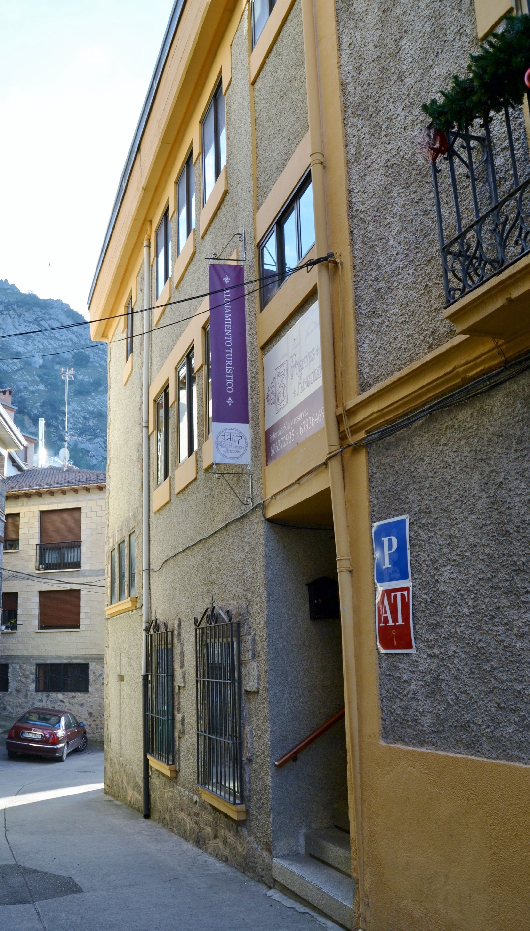 A building with a yellow facade, a visible staircase, and a parking sign.