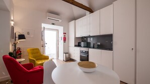 A modern kitchen with white cabinets, a microwave, and a stove. There is a red chair and a yellow chair in the dining area. - Soul House - Exclusive Apartment - Your Home away from Home (Lisboa)