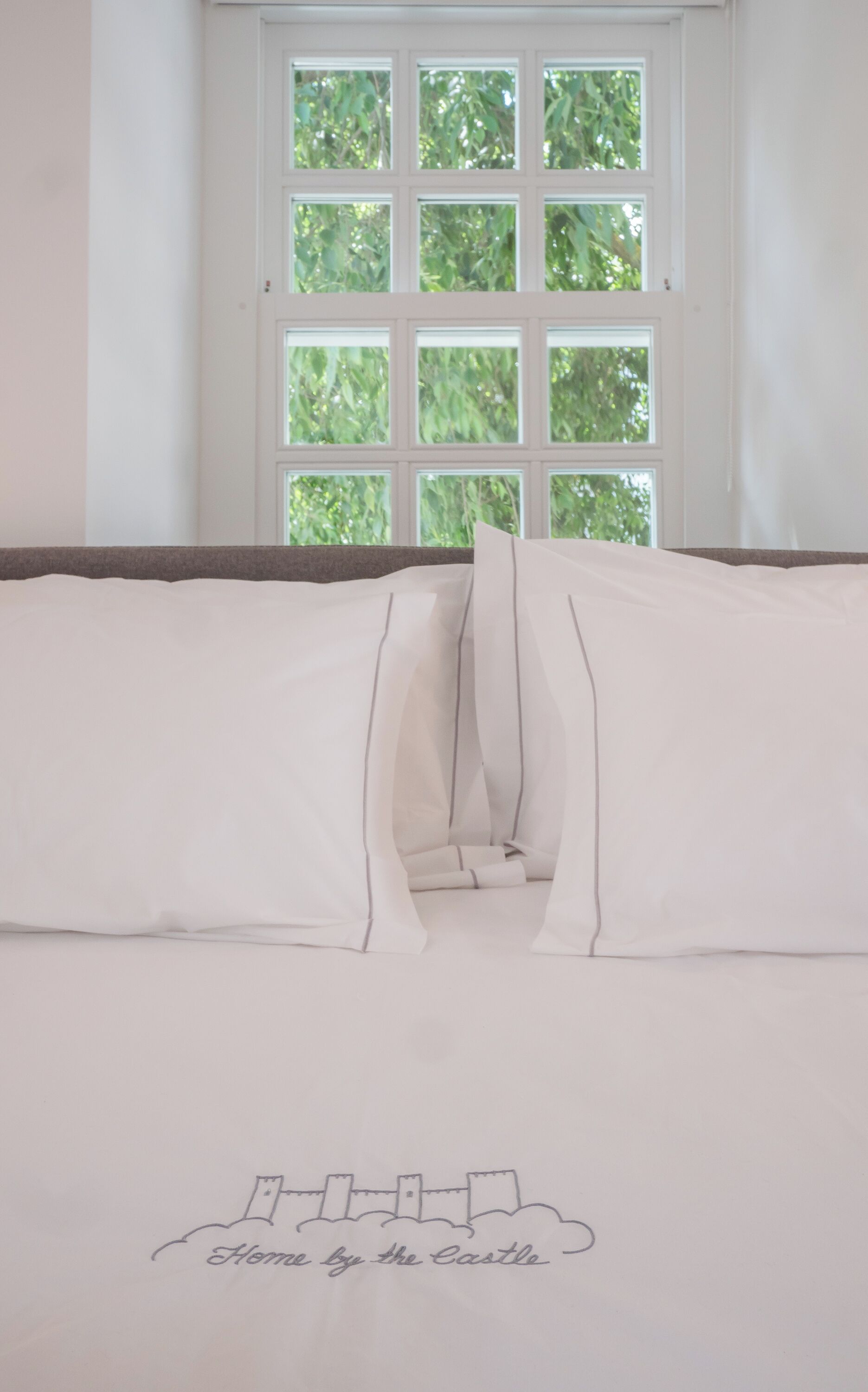 A neatly made bed with white linens and a pillow with a castle drawing.