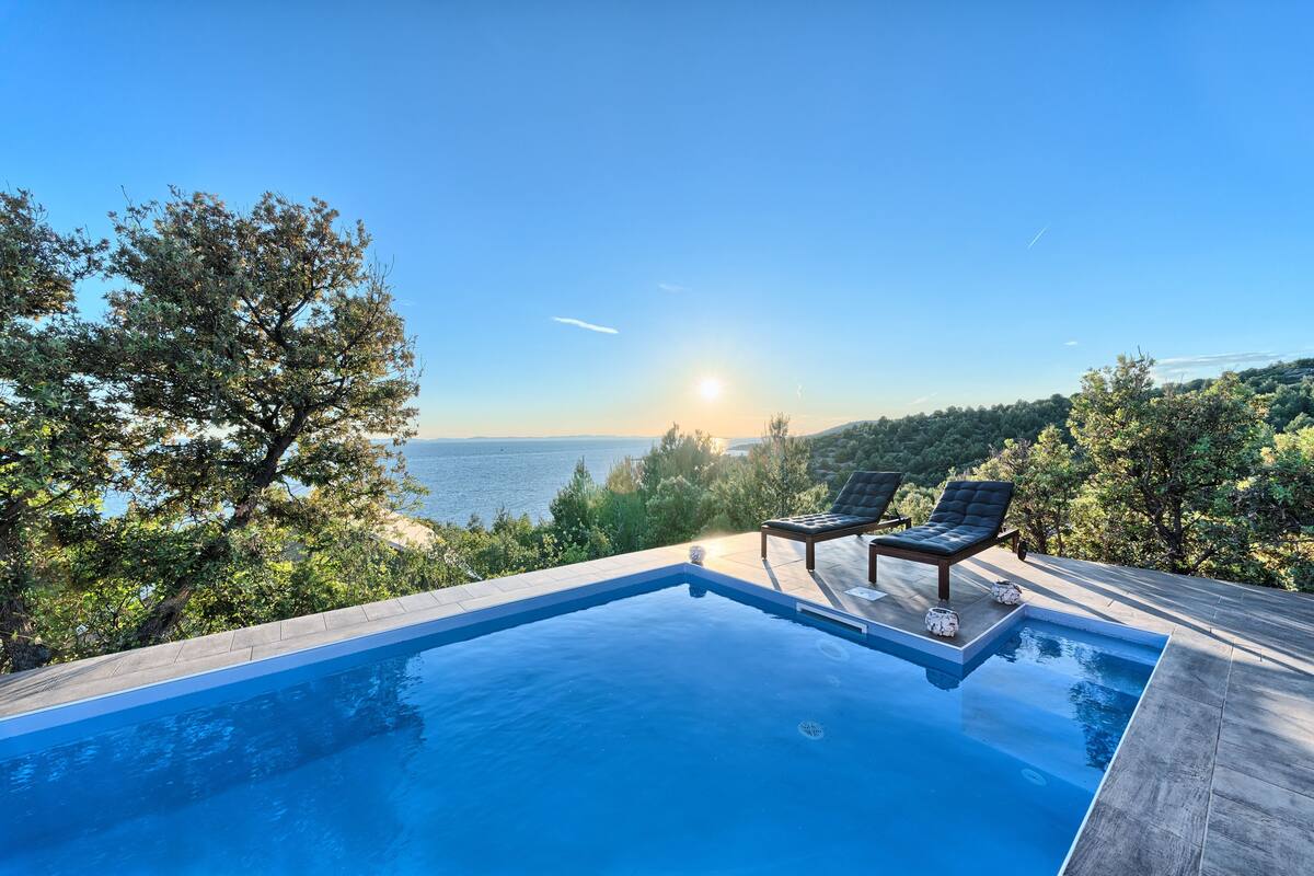 A swimming pool with two lounge chairs and a view of the sea.