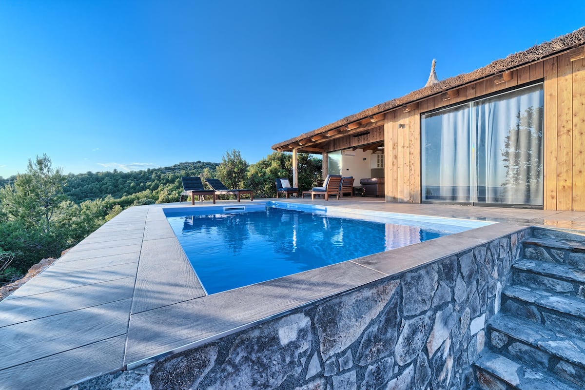 A modern pool area with a stone edge, wooden deck, and a view of the surrounding landscape.