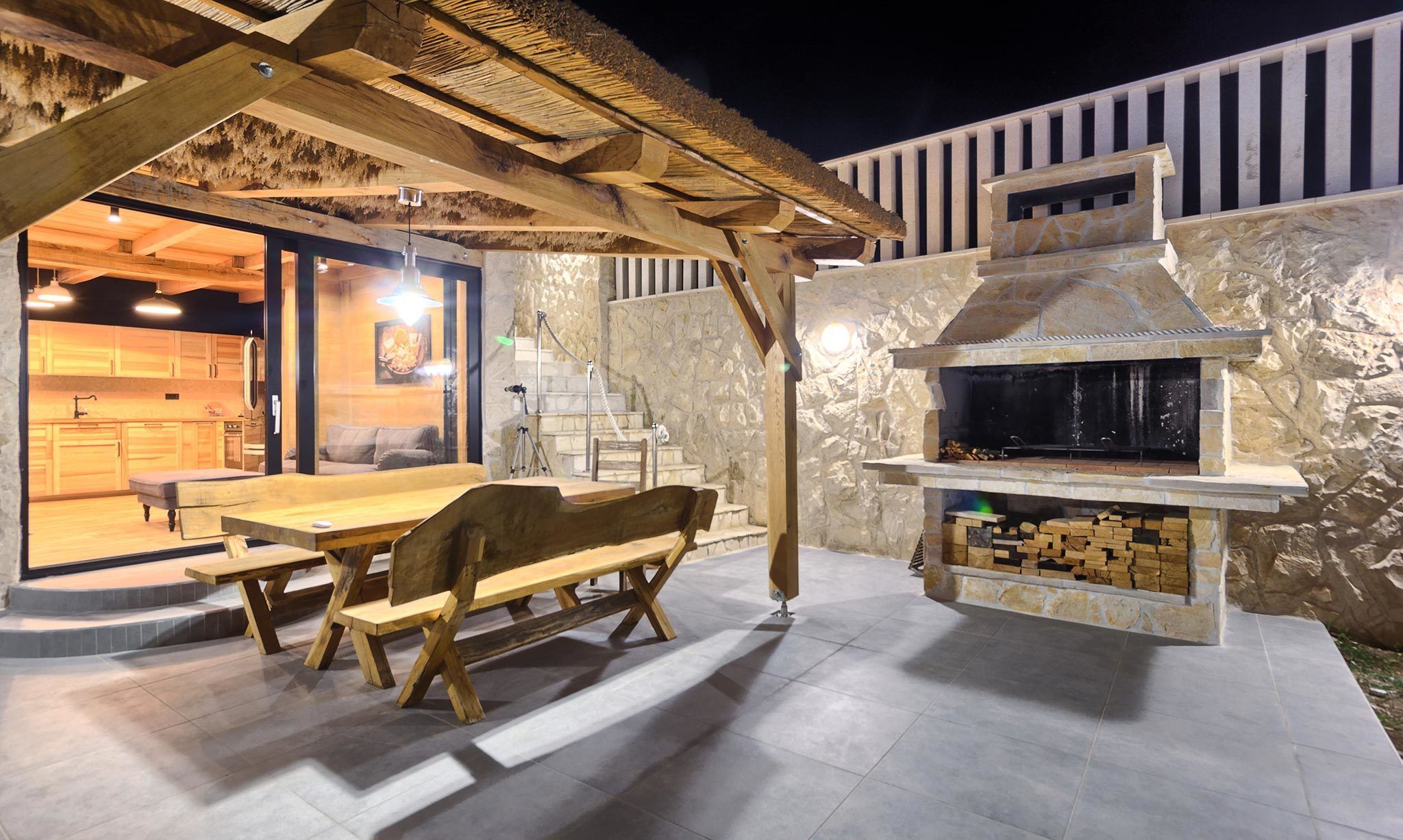An outdoor patio with a stone fireplace, wooden furniture, and a thatched roof structure.