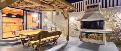 An outdoor patio with a stone fireplace, wooden furniture, and a thatched roof structure.