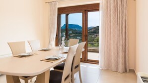 A dining area with a table set for four, large windows with curtains, and a view of a mountainous landscape.