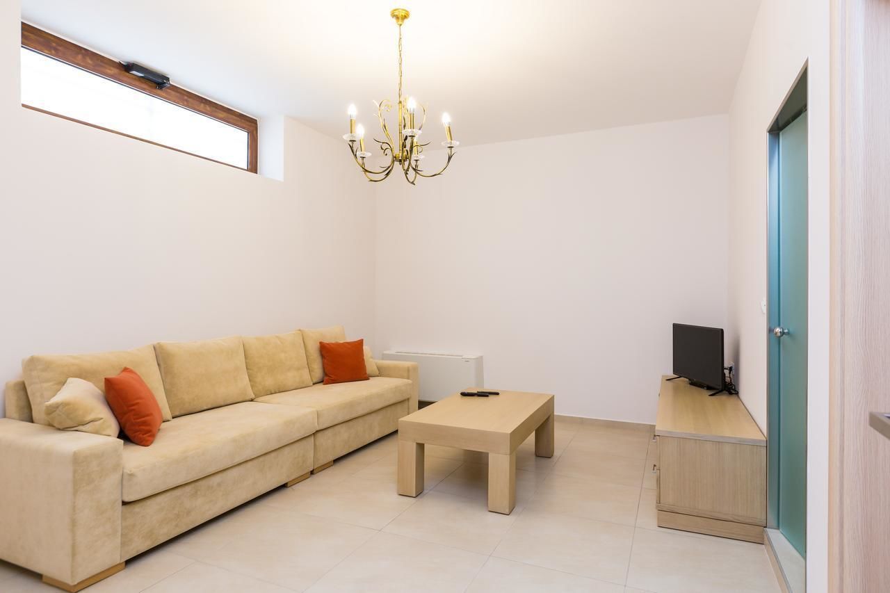 Ein Wohnzimmer mit einem beigefarbenen Sofa, einem Holztisch, einem Fernseher auf einem Holzständer und einer Chandelüster.