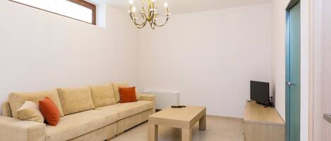 Ein Wohnzimmer mit einem beigefarbenen Sofa, einem Holztisch, einem Fernseher auf einem Holzständer und einer Chandelüster.