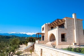 A modern two-story house with a stone facade, a covered patio, and a view of snow-capped mountains.
