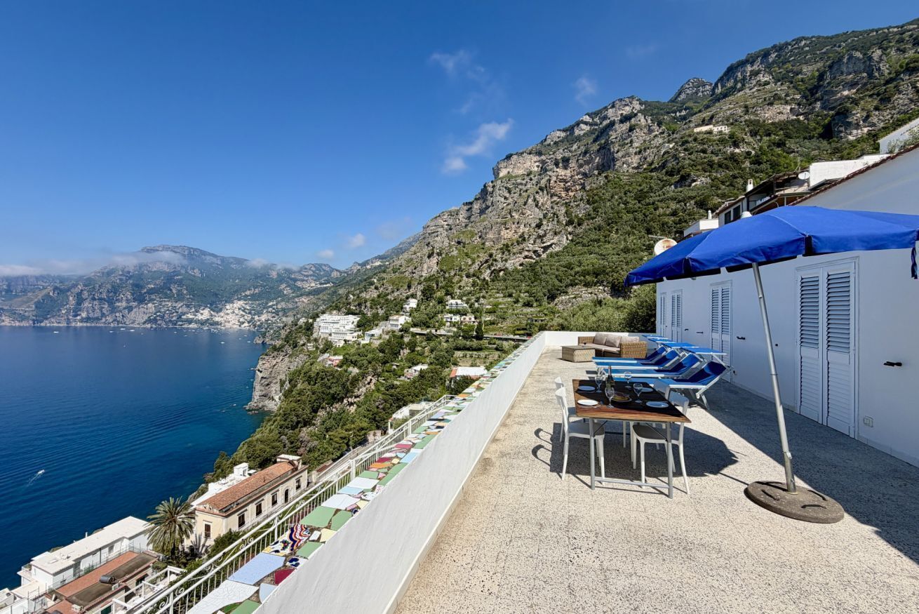 Une terrasse avec des sièges extérieurs, une vue sur la mer et un paysage montagneux en arrière-plan.