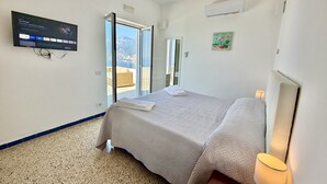 A bedroom with a bed, a TV mounted on the wall, a window, and a door leading to a balcony. - My Shazzy Praiano amazing Sea View, look on Capri and Positano (Praiano)