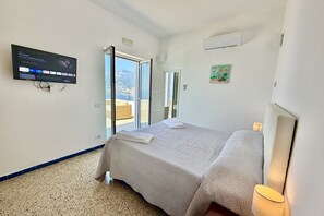 Une chambre à coucher avec un lit, un téléviseur fixé au mur, une fenêtre et une porte donnant sur un balcon.