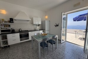 Une cuisine avec une table et des chaises, une vue sur la mer par une porte vitrée et un balcon avec une table et des chaises.