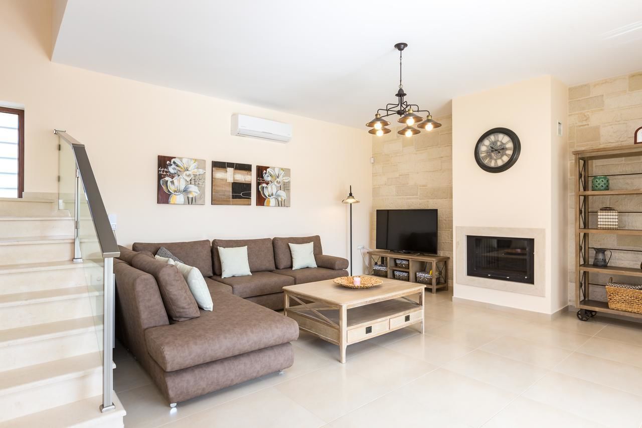 A modern living room with a sectional sofa, a coffee table, a fireplace, a television, and a staircase.