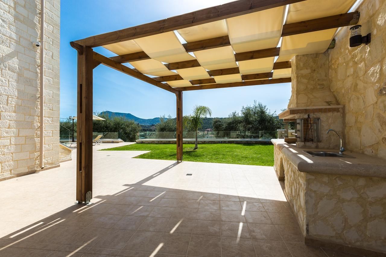 An outdoor patio with a stone wall, a wooden pergola, and a stone counter with a sink.