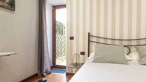 Een slaapkamer met een bed, nachtkastje, lamp, deur naar een buitenruimte en een wandplank.