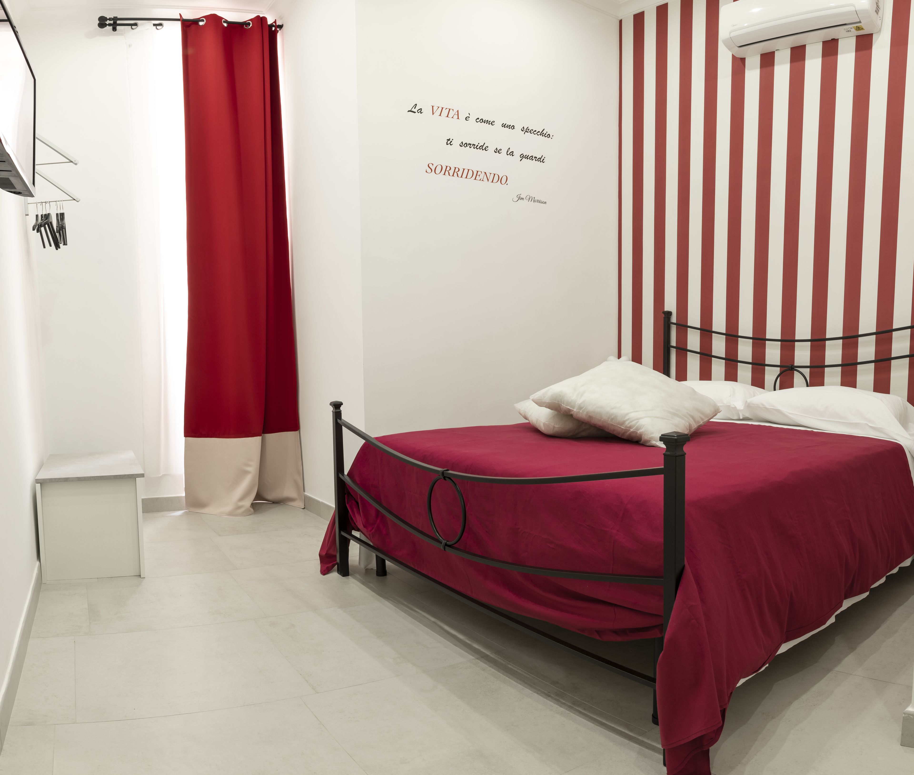 Een slaapkamer met een bed, een rood gordijn, een wandairconditioner en een citaat op de muur.