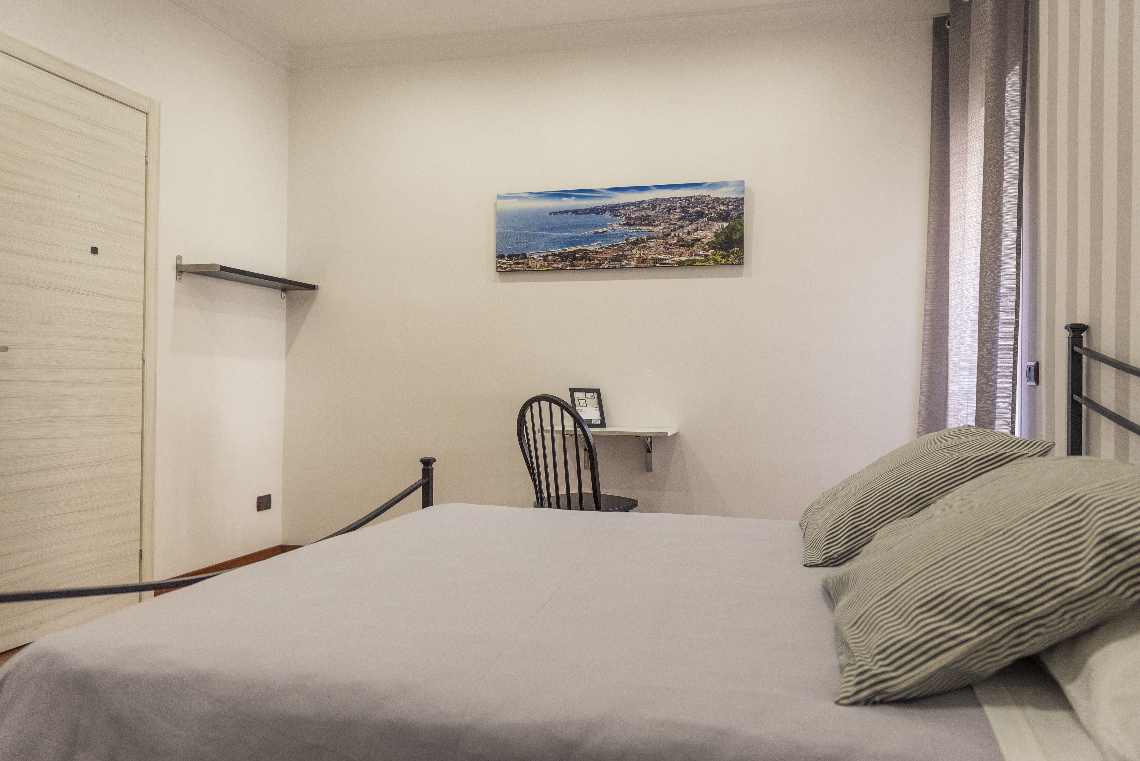 A bedroom with a bed, a chair, a shelf with a picture, and a door.