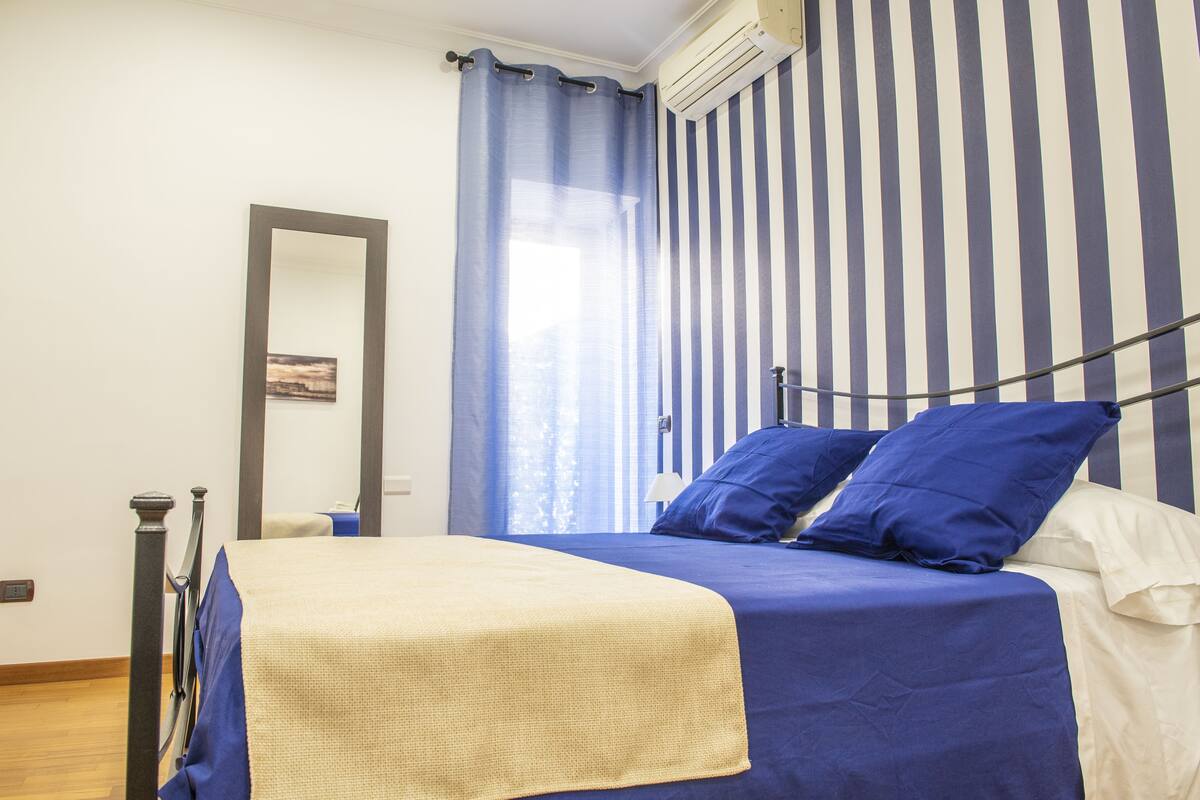 A bedroom with a bed, a mirror, and a window with curtains.