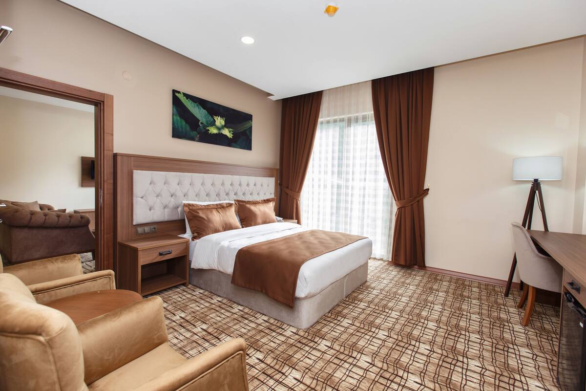 A hotel room with a large bed, a desk, a chair, a mirror, and a painting on the wall.