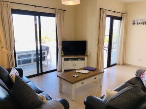 A living room with a sofa, a coffee table, a television, and a sliding glass door leading to an outdoor area. - A Relaxing, Perfectly located 4 bed Villa in Coral Bay (Peyia)