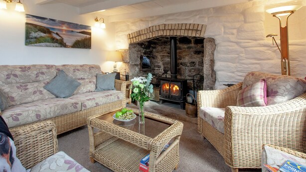 A cozy living room with a stone fireplace, wicker furniture, and a painting on the wall. - 3 bedroom accommodation in Nanpean, near St Austell (Nanpean, near St Austell)