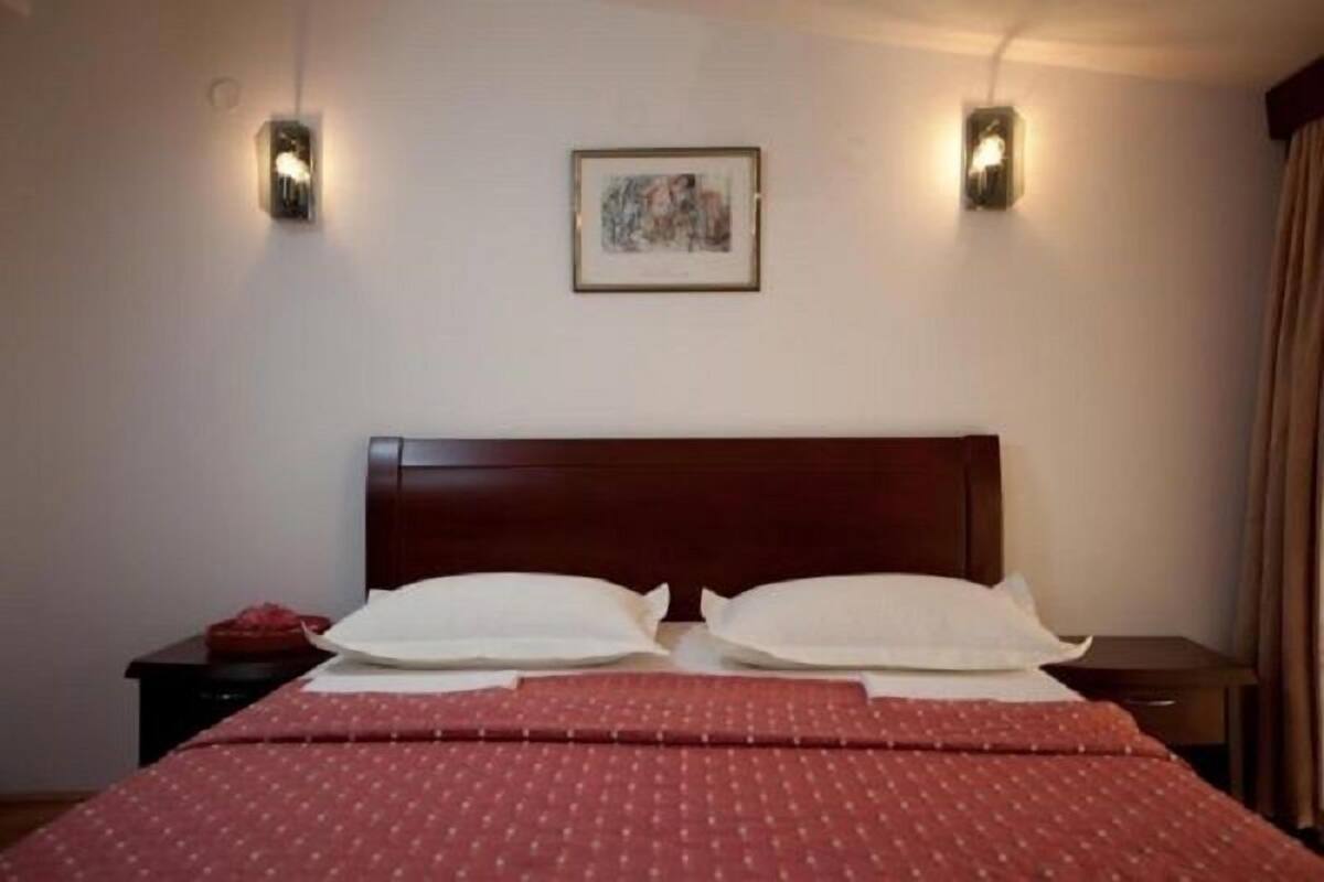 Une chambre d’hôtel avec une tête de lit en bois, deux tables de chevet, un lit avec une literie rouge et deux appliques murales.