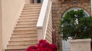 A building with a staircase leading to a door, a stone wall, and a balcony with potted plants. - Apartments Begic (Makarska)