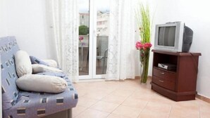 A room with a sofa, a television on a wooden stand, and a view through a glass door. - Apartments Begic (Makarska)