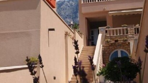 A multi-story hotel with balconies, a staircase, and a mountain view. - Apartments Begic (Makarska)