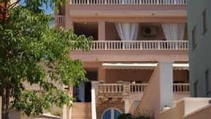 A multi-story hotel with a central staircase leading to the entrance, surrounded by greenery and a clear sky. - Apartments Begic (Makarska)