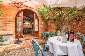 An outdoor patio with a brick wall, a table set with wine glasses and bottles, and a blue chair. - old barn on Via Francigena (Siena)
