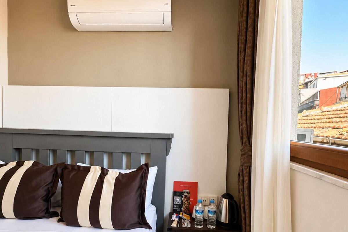 A hotel room with a bed, bedside table, and an air conditioning unit.