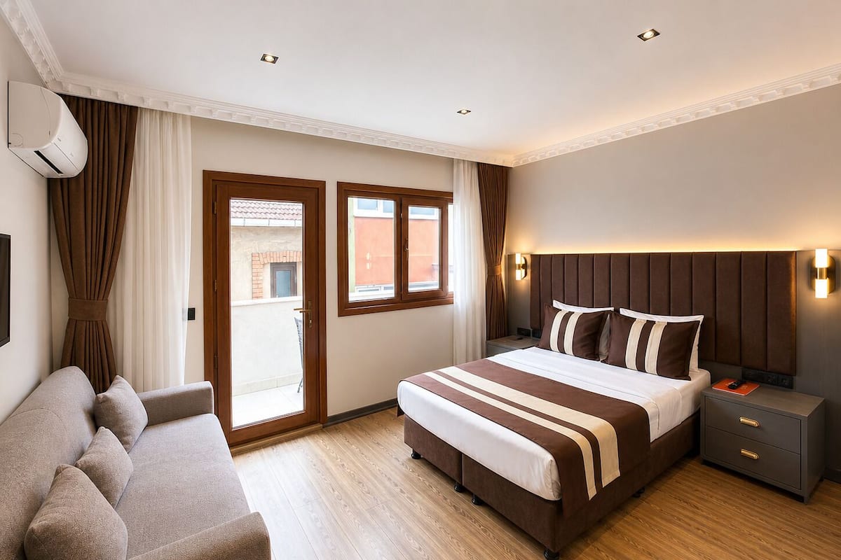 A hotel room with a bed, a sofa, a nightstand, and a window.