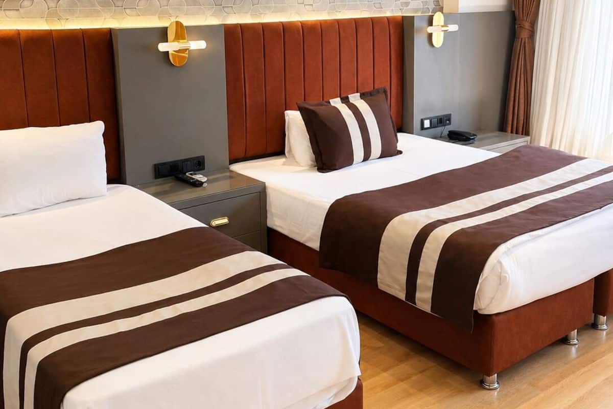 A hotel room with two beds, a modern headboard, bedside tables, and a decorative wall panel.