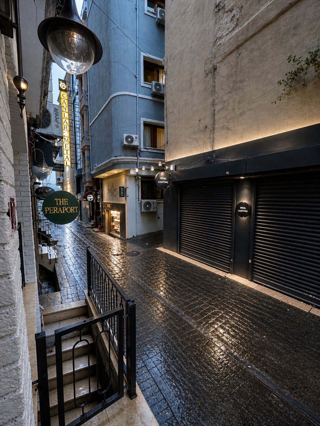 A narrow alleyway with a staircase leading to a building. There are signs for 'The Peraport' and 'Rival Lighting' visible.